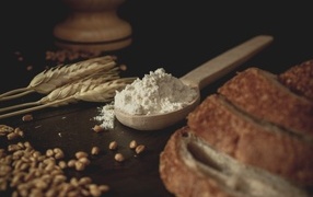 Spoon of flour on the table with wheat and bread