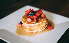Pancakes with strawberry pieces, honey and blueberries on a plate