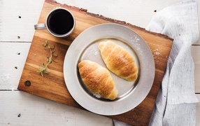 Два круассана на тарелке с чашкой кофе