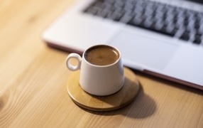 A cup of strong coffee stands by the laptop