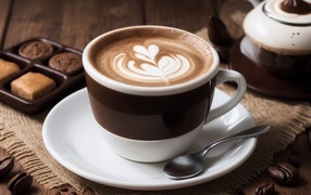 Чашка кофе с рисунком на пене на столе с конфетами