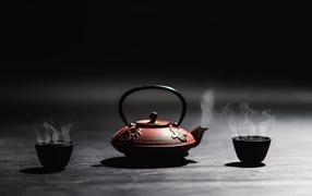 Kettle with hot tea on black background