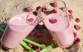Two glasses of berry smoothie with raspberries on the sand