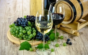 Two glasses of wine on a table with grapes and a barrel