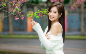 Красивая азиатка в белом свитере стоит у ветки дерева