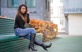 A brunette in blue jeans sits on a bench