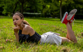 Темнокожая девушка в белой юбке лежит на траве