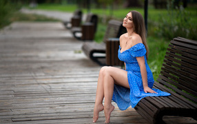 Девушка в красивом голубом платье сидит на лавке в парке