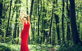 A girl in a beautiful red dress stands in the forest