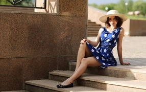 Девушка в синем платье в белый горох сидит на ступеньках