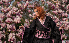 Девушка в кимоно стоит у куста с цветами магнолии