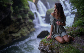 Девушка в рубашке сидит у водопада