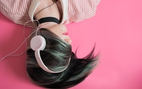 A girl in headphones lies on a pink floor