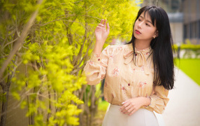 Молодая девушка азиатка стоит у дерева с зелеными листьями