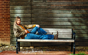 A young girl in blue jeans lies on a bench