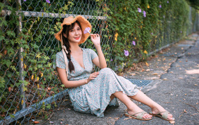 Asian girl in a dress sits by the fence