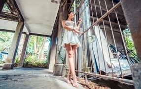 Девушка азиатка в платье стоит у решетки 