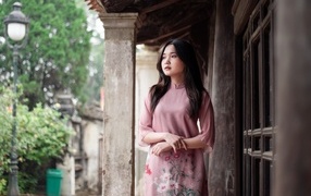 Девушка азиатка в розовом платье стоит у дома