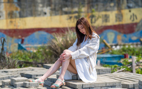 Девушка азиатка в белой рубашке сидит у воды