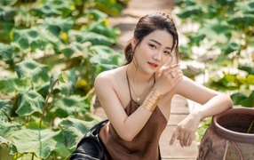 Девушка азиатка сидит у зеленых листьев лотоса