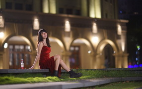 Азиатка в длинном красном платье сидит на ступенях