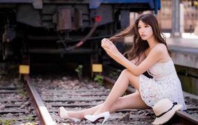Красивая девушка азиатка в белом платье  сидит на рельсах