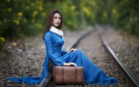 Beautiful Asian girl sits on the rails with a suitcase