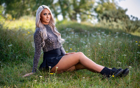 Красивая блондинка в юбке сидит на траве