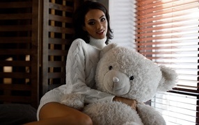 Красивая девушка в свитере с медведем у окна