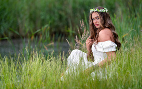 Красивая девушка в белом платье с венком на голове у пруда 