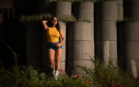 Красивая девушка в очках стоит у стены