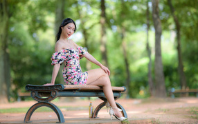 Милая девушка азиатка в платье сидит на лавке в парке