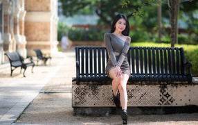 Cute Asian girl in a gray dress sitting on a bench