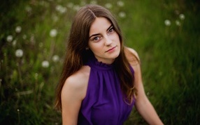 Милая девушка в фиолетовом платье сидит на траве