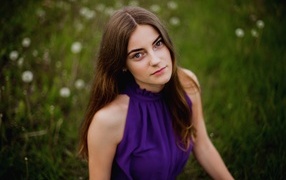 Милая девушка в фиолетовом платье сидит на траве