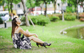 Мечтательная девушка азиатка сидит на траве в парке