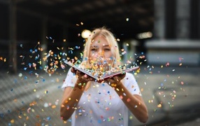 Девушка сдувает конфетти с книги 