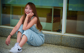 Девушка в джинсовом комбинезоне сидит на полу