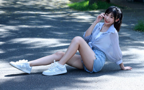 Улыбающаяся девушка азиатка в кедах сидит на дороге