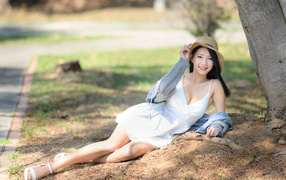 Улыбающаяся азиатка в белом платье лежит под деревом