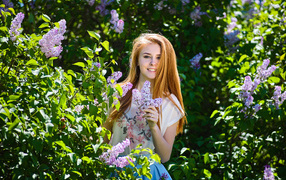 Улыбающаяся девушка стоит у куста сирени