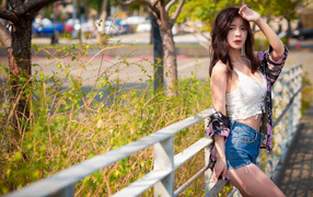 Молодая азиатка в синих шортах стоит у забора