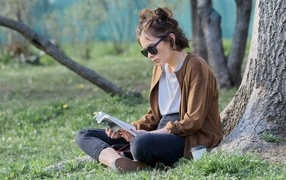 Молодая девушка сидит под деревом с книгой