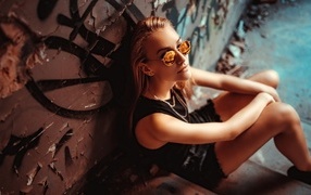 Young girl with glasses sitting against the wall