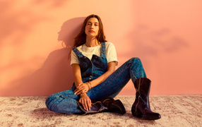 Американская модель Хейли Болдуин в джинсовом комбинезоне сидит у стены