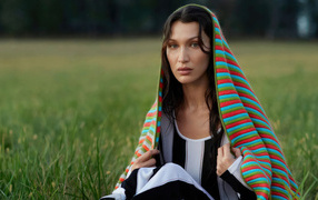 Model Bella Hadid covered with a blanket sits on the grass