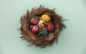 Красивые разноцветные яйца в гнезде из перьев на сером фоне