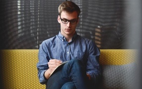 Мужчина в очках сидит с книгой на диване