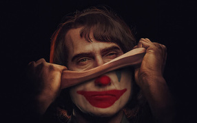Joker takes off his mask on a black background