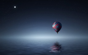 Big hot air balloon flies over the water at night